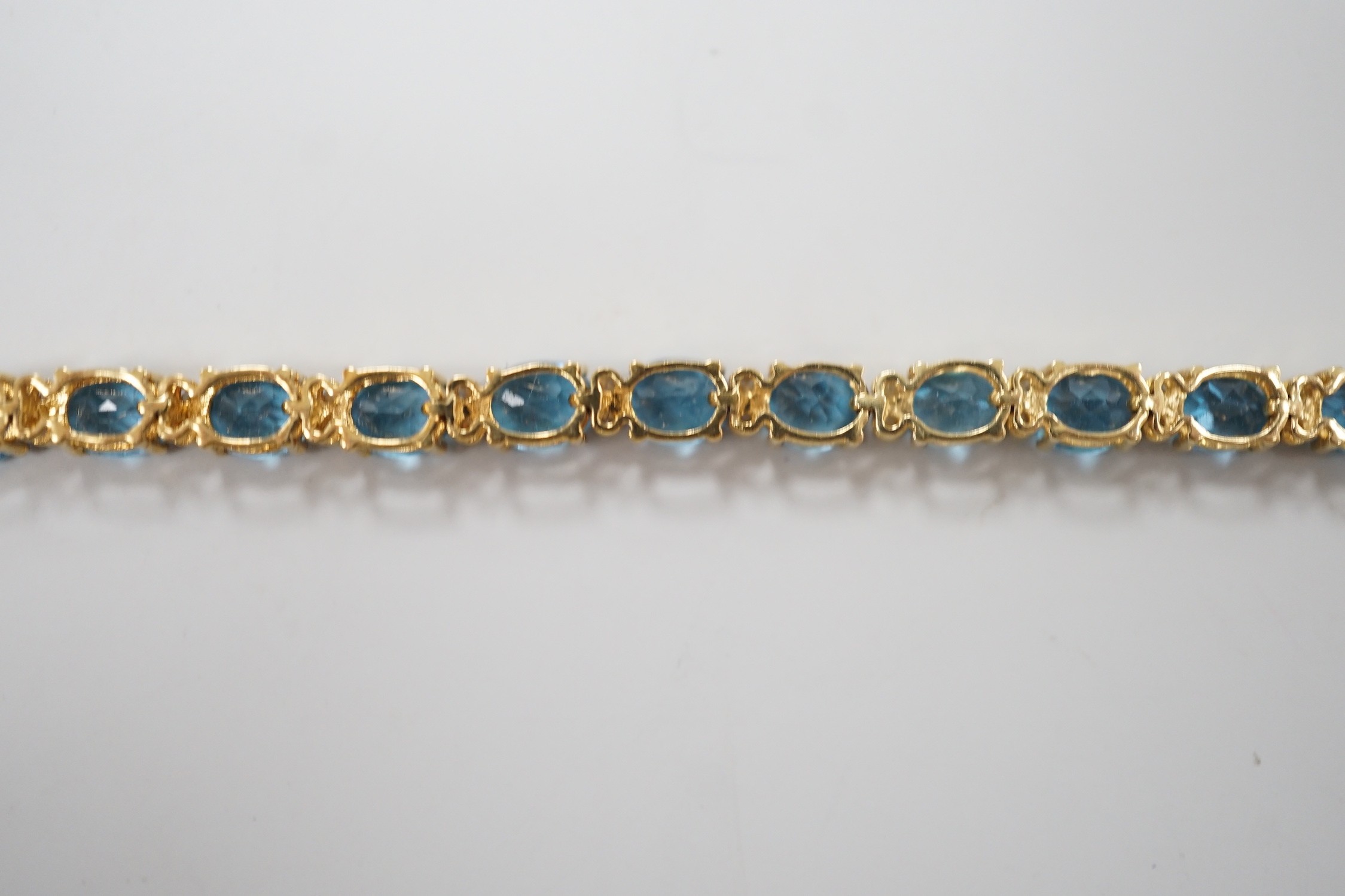 A modern 750 yellow metal and blue topaz set line bracelet, with diamond chip spacers, 17.75cm